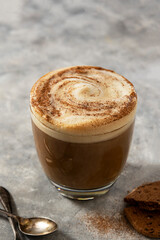 Glass of coffee drink with whipped milk, latte hot drink on gray background.