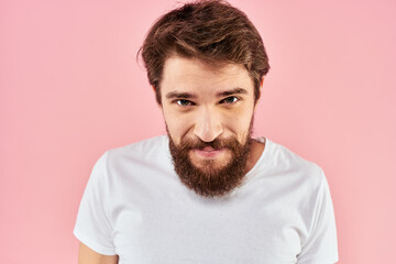 Bearded man in white t-shirt gesturing with hands facial expression close up pink background