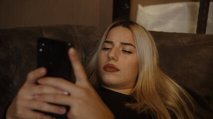 Young unhappy blonde woman lying on sofa received a bad message or had a bad incident on the phone