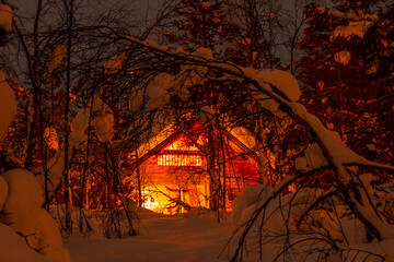 Light in a Wooden House in a Night Winter Forest