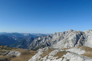 Obraz premium A panoramic view on the plain on top of a mountain in Hochschwab region in Austrian Alps. The flora overgrowing the slopes is turning golden. Autumn vibes. Many mountain chains in the back. Wilderness