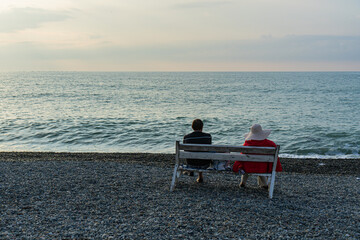 a man and a woman sit on a bench by the Black Sea and watch the sunset