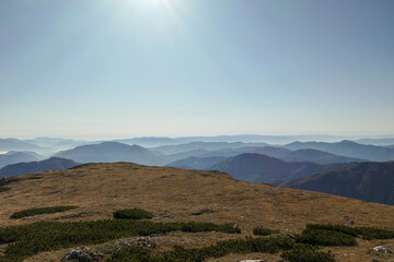 Fototapeta premium A panoramic view on the plain on top of a mountain in Hochschwab region in Austrian Alps. The flora overgrowing the slopes is turning golden. The valley is shrouded in fog. Mysterious landscape