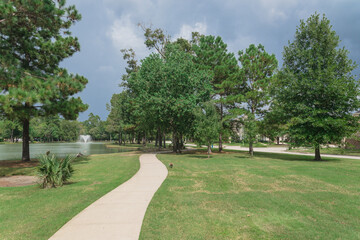 Empty concrete pathway thru neighborhood park with water fountain and ducks swimming in Houston, Texas, USA