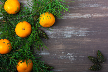 Tangerines with fir and pine branches and cones on a brown wood background. Postcard for Christmas and New Year. Top view