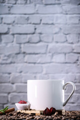 White cup full of coffee beans , red flowers and red chocolate candy against the background of a dark brick wall. Morning espresso. Coffee mug.	