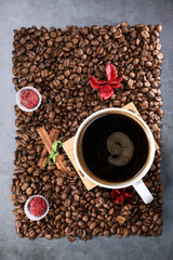 Flat lay view of a white cup full of coffee beans in the form of a photo frame with red chocolate candy and red flowers. Morning espresso. Coffee mug.