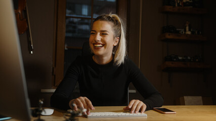 Young blond beautiful woman dressed in black spends time on the computer at the desk in the office, Office worker concept