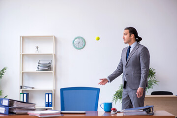 Young male employee juggling with tennis ball in the office