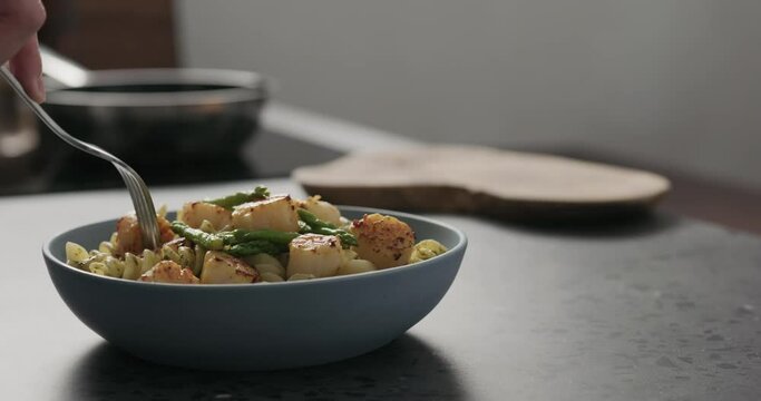 Slow motion add asparagus to pesto fusilli with scallops in blue bowl on concrete countertop