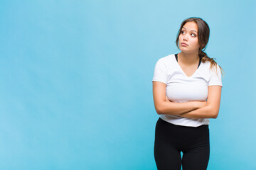 young hispanic woman with a worried, confused, clueless expression, looking up to copy space,...