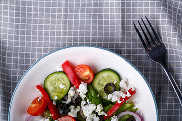 Half a light plate of Greek salad on a checkered napkin with a fork.