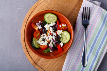 beige plate of Greek salad on a gray background on a gray napkin with a fork.
