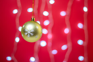 Fototapeta premium Yellow Christmas ball on a background of a glowing garland. Christmas decorations on a red background. Holiday decorations. Christmas concept. 
