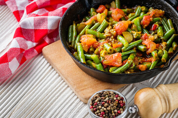 stewed green beans in a cast iron skillet on a white wooden rustic background