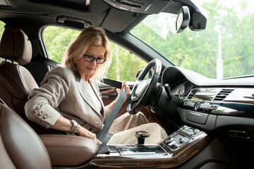 Fototapeta na wymiar Mature businesswoman in elegant casualwear sitting in car and fastening seatbelt