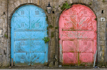 Pair of large  colourful old doors with peeling paint set in a stone building. - 392476208