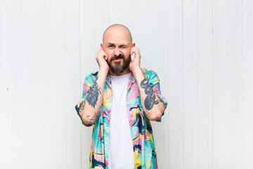 bald man looking angry, stressed and annoyed, covering both ears to a deafening noise, sound or...