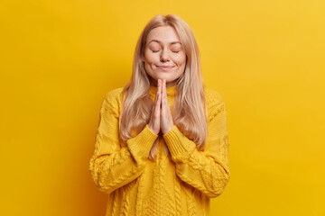 People and faith concept. Calm beautiful blonde woman keeps hands pressed together in pray closes...