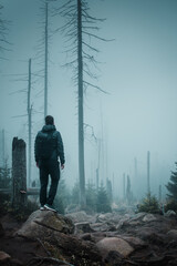 Back view of a hiking adventure man standing on rocks of a mountain scene with moody dark foggy...