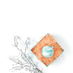 The decorative ball is in a box with yellow paper straw. Nearby is a snow-covered branch with white berries. Minimalistic template for christmas, new year, invitation, banner. Flat lay, copy space.