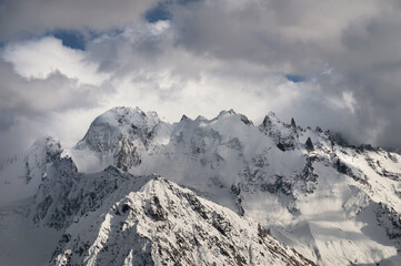 Fototapeta na wymiar Snow-capped peaks of the Caucasian high mountains in the evening. Dramatic sky