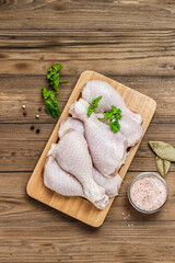 Chicken legs with herbs and spices on wooden background. Top view, flat lay, space for text.