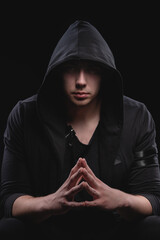A large man in a hood and a black sweater with hands in a gesture of strength. Studio portrait with...
