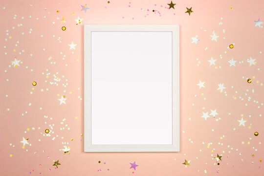 Festive background with blank white photo frame on peach backdrop. Mock up for photo or text. Top view.