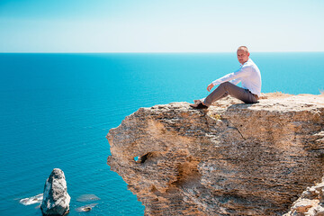A pensive young man sits at a cliff. Portrait of a guy by the sea.