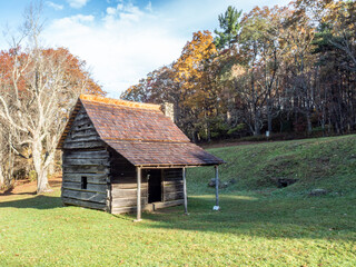Fototapeta na wymiar Rustic cabin sits amidst the beautiful autumn foliage and early morning sunlight.