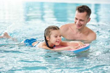 Happy young father teaching his adorable little daughter to swim in pool