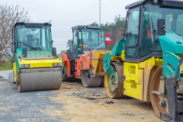 Asphalt paver machine and steam road roller during road construction and repairing works, process of asphalting and paving, workers working on the new road construction site