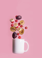 Fruits fly into the white Cup-raspberries, plums, bananas, on a pink background. Food levitation. Vertical orientation