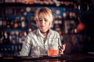 Focused girl tapster intensely finishes his creation while standing near the bar counter in pub