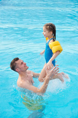Happy young man playing with his adorable little daughter in swimming pool