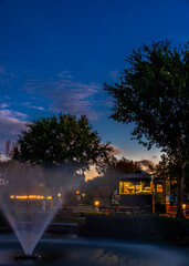 Fototapeta premium Evening at the Rv park under a sunset sky in front of a water fountain with lights on the interior of the coach