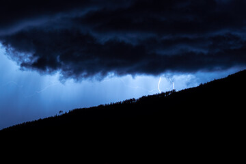Night time image of threatening storm clouds with lightning over the mountains