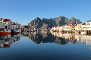 Boats in Henningsvaer harbor with mountain in background  - obrazy, fototapety, plakaty