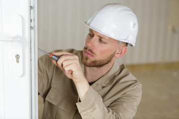 young male contractor using screwdriver on a door lock mechanism