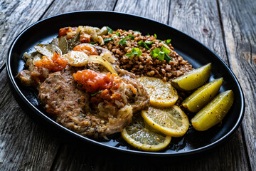Roasted meat, buckwheat and pickled cucumbers lemon and toamtoes on wooden table
