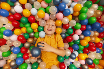 Happy child laying in pool and playing with colored balls in the park