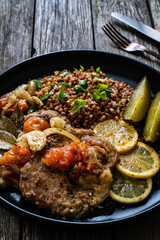 Roasted meat, buckwheat and pickled cucumbers lemon and toamtoes on wooden table
