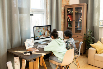 Schoolkids sitting in front of computer monitor and listening to their teacher