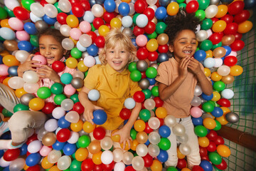 Fototapeta na wymiar High angle view of group of happy children smiling at camera while lying among colored balls in the pool