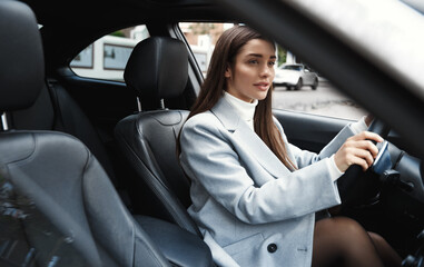 Fototapeta na wymiar Elegant woman driving her car, looking at rear window. Businesswoman driver going on a meeting