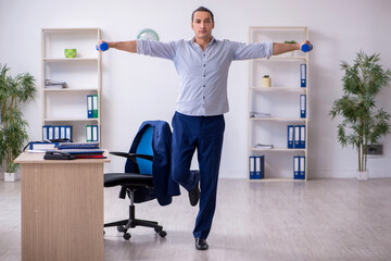 Young handsome male employee doing exercises in the office