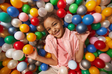 Fototapeta na wymiar Portrait of African happy girl smiling at camera lying in the pool with balls