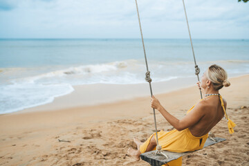Young woman in yellow dress swing on swing on the beach