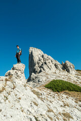 A man standing on top of a sharp, pointy boulder in Hochschwab region, Austrian Alps. The steep mountain wall in front look very dangerous. High mountaineering. Autumn vibes. Adventure and freedom